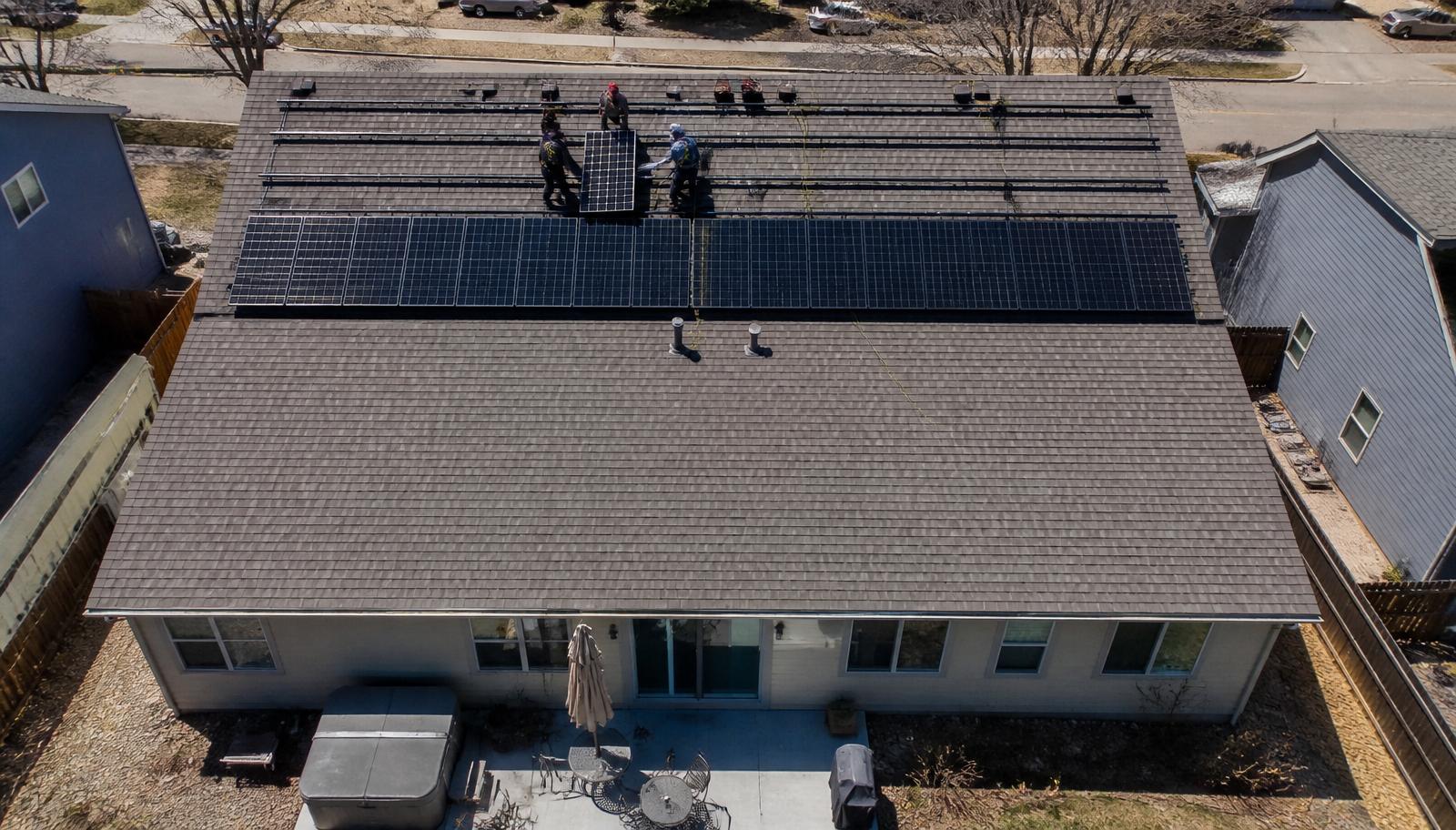 Overhead drone view of solar installers placing panels on the rear roof slope of a Colorado suburban home